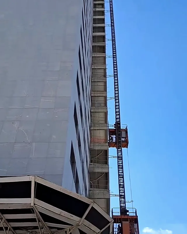Prédio alto em construção com elevador de obra na fachada